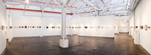 Panoramic view of a gallery exhibition with tiny canvases hung on the wall