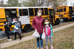 Mother and daughter stand in front of a school bus with a grab and go meal
