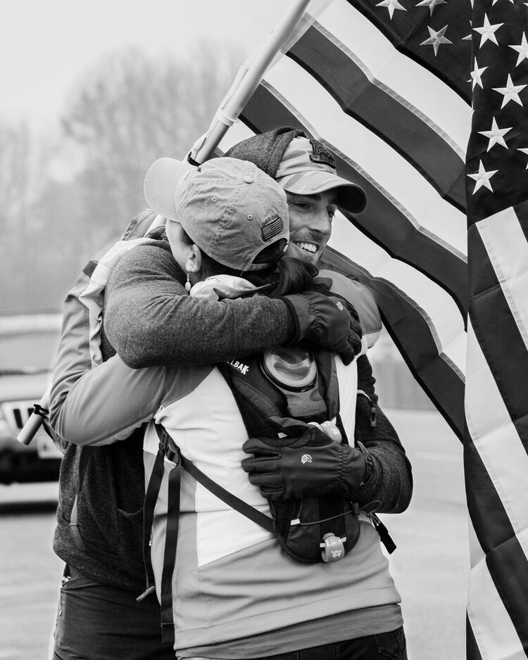 Vic Wise hugging a woman while he has his ruck sack on his back with a U.S. flag.