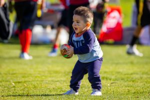 Toddler plays with football on a grassy field