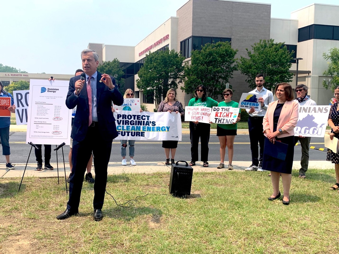 Environmentalists rally around a legislator with signs reading “protect Virginia’s clean energy future,” “do the right thing,” and “Virginians defend RGGI.”