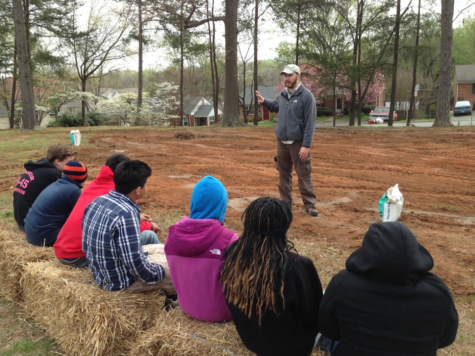 A man addresses a group of students in an outdoor setting
