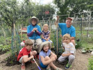 Two adults in blue shirts stand posed, smiling with a group of four children outside in a garden.