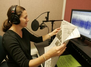 Woman reading newspaper into microphone