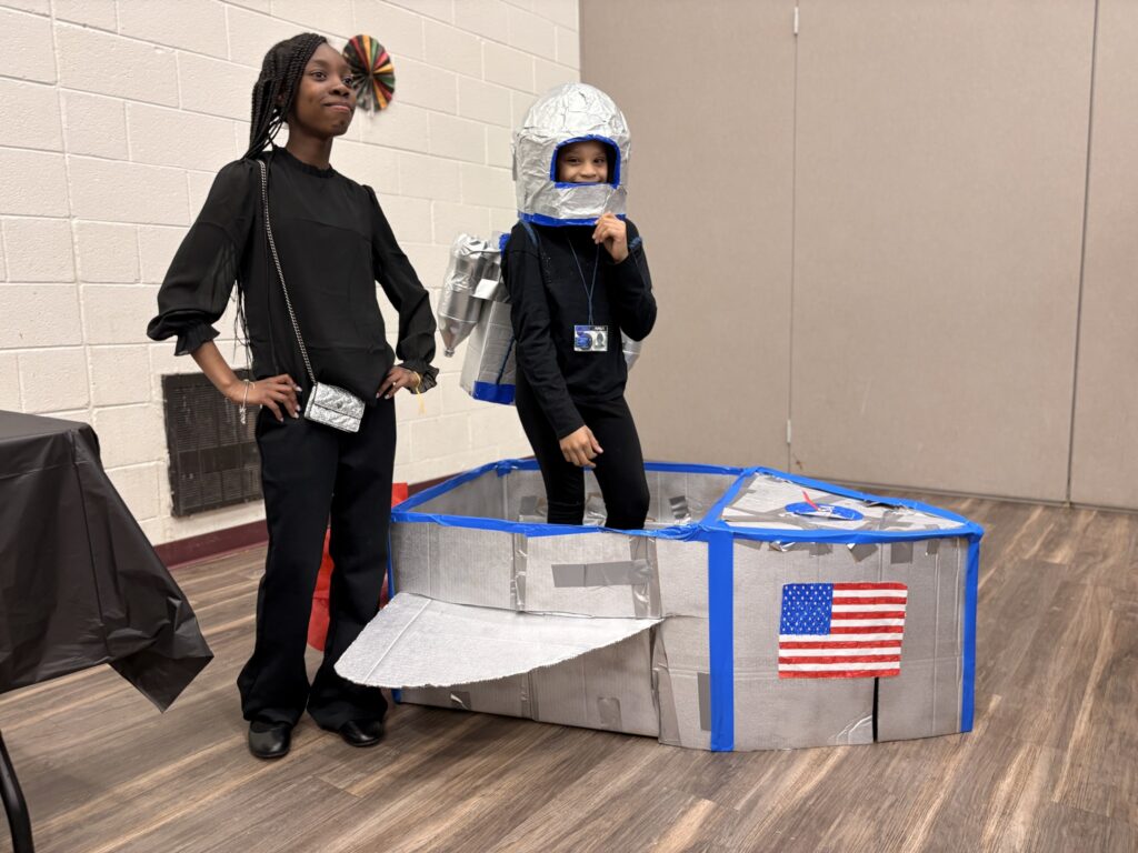 Children stand near spaceship model they created.