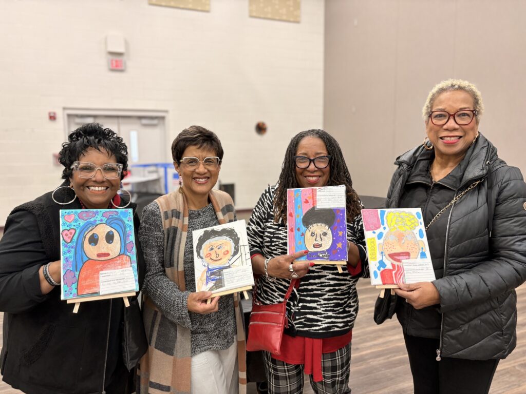 Four women hold painted photos of themselves
