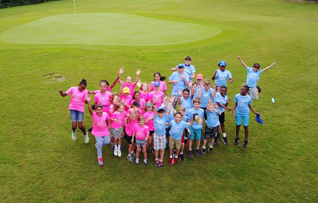 Group of kids in blue and pink t-shirts posing for a photo on the golf course