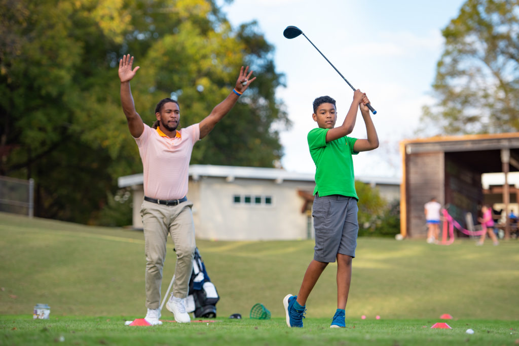 Boy swings golf club during lesson with teacher